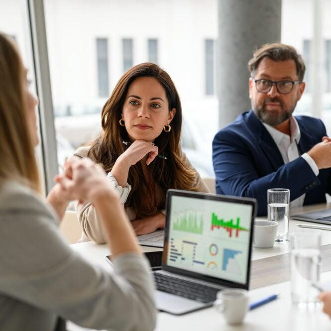 Female manager analyzing business graphs on laptop and discussing data with professional colleagues in meeting